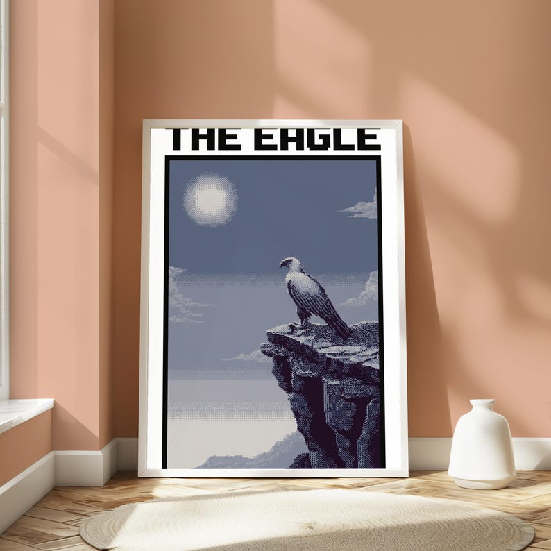May include: A framed pixel art poster titled THE EAGLE, featuring a white and grey eagle perched on a dark rocky cliff against a blue sky with a bright sun, clouds, and a distant horizon line, all rendered in a distinct digital block style.