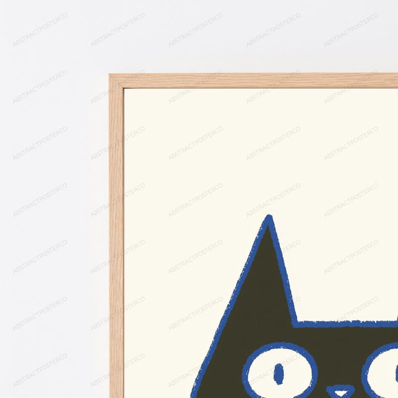 May include: A framed wall art print featuring a stylized black cat head with large white eyes and a blue outline. The cat is set against a cream-colored background, and the artwork is enclosed in a light-toned wooden frame with a clean, simple border.