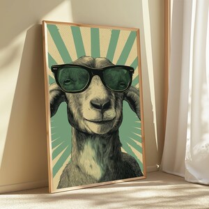 May include: A framed wall art print featuring a detailed illustration of a goat wearing black sunglasses. The background consists of a light green and cream-coloured sunburst pattern with a subtle dot texture, all enclosed in a light wood frame.