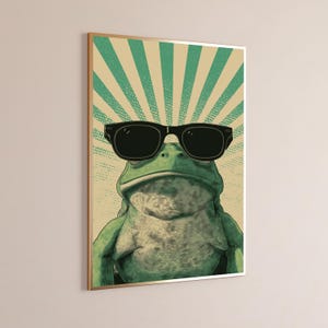 K&ouml;nnte beinhalten: Ein gerahmter Wandkunstdruck, der einen gr&uuml;nen Frosch mit einer gro&szlig;en schwarzen Sonnenbrille zeigt. Der Hintergrund besteht aus einem beigen und gr&uuml;nen Sonnenstrahlenmuster mit punktierter Textur. Der Frosch ist mittig platziert.