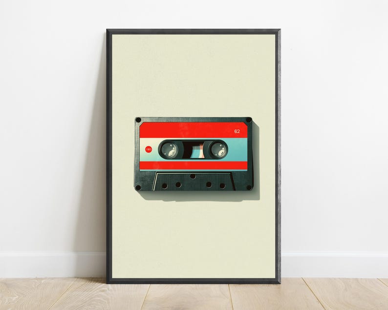 May include: A framed wall art print featuring a centered cassette tape with a black plastic shell, a bright red top section, and a light blue middle band. The number 62 is printed in white on the top right corner of the red section.