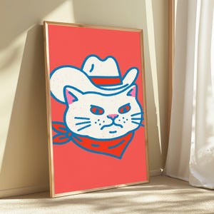 May include: A framed wall art print featuring a stylized illustration of a white cat wearing a white cowboy hat with a red band and a red bandana around its neck. The cat has a grumpy expression, outlined in blue, set against a solid coral background.
