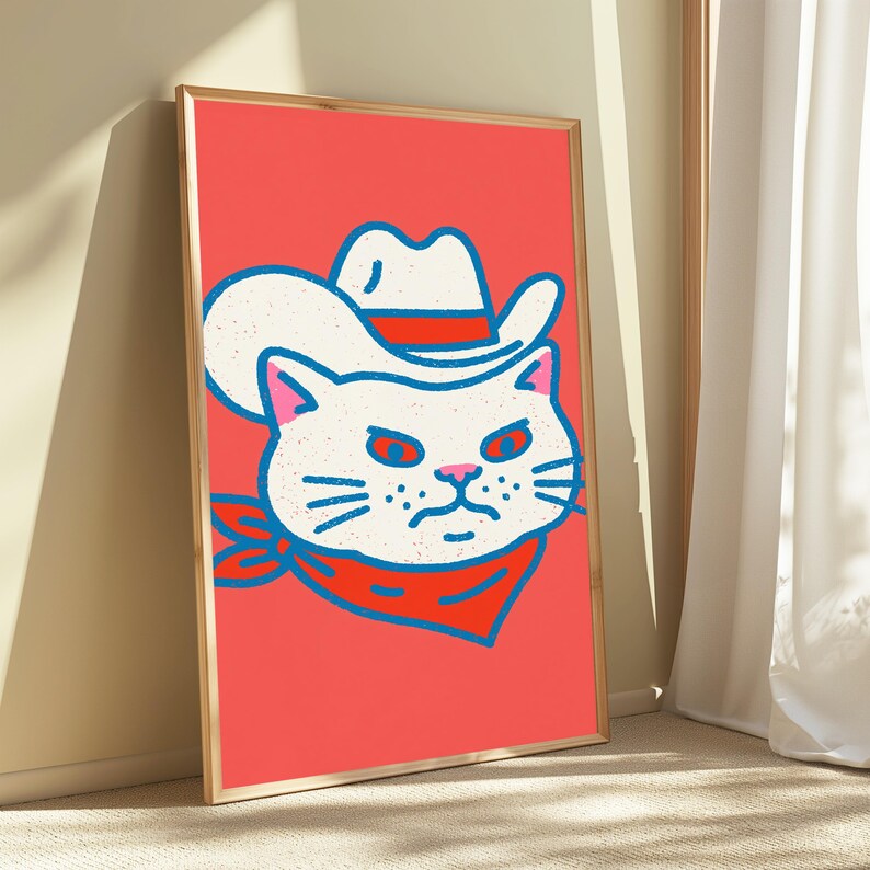 May include: A framed wall art print featuring a stylized illustration of a white cat wearing a white cowboy hat with a red band and a red bandana around its neck. The cat has a grumpy expression, outlined in blue, set against a solid coral background.