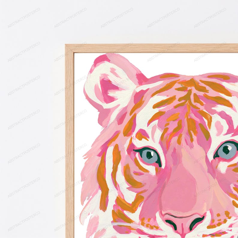 May include: A framed wall art print featuring a stylized tiger head painted in shades of pink, white, and orange. The tiger has light blue eyes and a dark nose, set against a white background within a light-colored wooden frame.