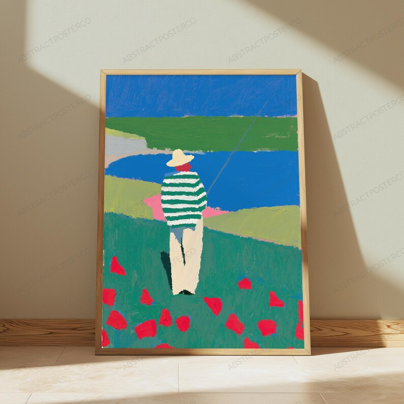 Op de afbeelding: Een ingelijste kunstdruk met een gestileerd schilderij van een persoon met een strooien hoed en een groen-wit gestreept shirt, staand in een veld met rode bloemen. De achtergrond toont een blauw wateroppervlak, groene heuvels en een blauwe lucht.