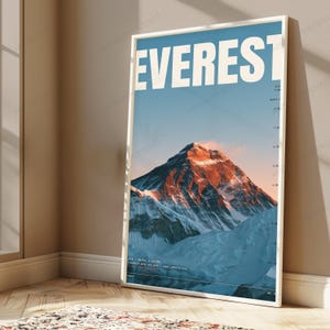 Op de afbeelding: Een verticale wandkunstprint met een foto van de Mount Everest en de tekst EVEREST in grote witte letters bovenaan. De bergtop wordt verlicht door warm zonlicht tegen een blauwe lucht, met hoogtemarkeringen aan de rechterkant.