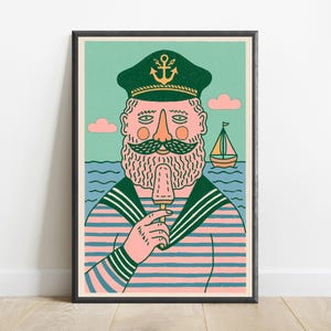 K&ouml;nnte beinhalten: Ein gerahmter Kunstdruck zeigt einen b&auml;rtigen Seemann mit einer dunkelgr&uuml;nen M&uuml;tze mit goldenem Ankeremblem und einem rosa-blau gestreiften Hemd. Der Seemann h&auml;lt ein hellbraunes Eis am Stiel. Der Hintergrund zeigt ein blaues Meer und ein Segelboot.