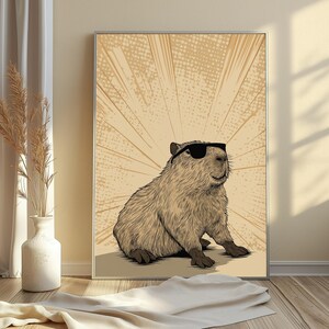 May include: A framed wall art print featuring a detailed illustration of a capybara wearing black sunglasses. The capybara is rendered in shades of brown against a light tan background with a radiating sunburst pattern and a dotted texture.