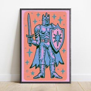 May include: A framed art print featuring a stylized illustration of a knight in armor holding a sword and a shield with a star emblem. The figure is rendered in blue and pink tones against a peach background, surrounded by blue star shapes.