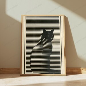 May include: A framed rectangular wall art print featuring a black silhouette of a cat sitting in profile. The cat is overlaid with horizontal black and cream-colored stripes that create a visual effect of light filtering through window blinds.