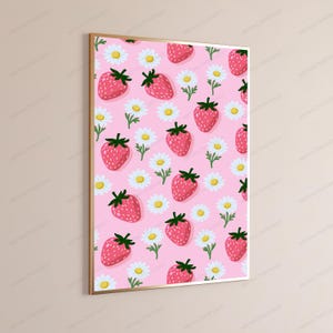 May include: A rectangular wall art print featuring a repeating pattern of pink strawberries with green stems and white daisies with yellow centers on a light pink background, enclosed within a thin metallic gold frame.