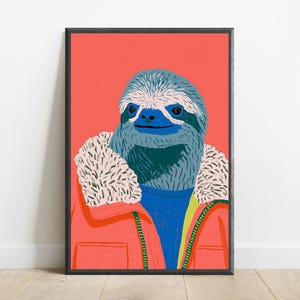 May include: A framed art print featuring a stylized illustration of a sloth with blue fur and a white face. The sloth wears a bright orange jacket with a white faux-fur collar over a blue sweater. The background is a solid, vibrant coral color.
