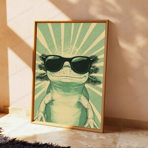 May include: A rectangular wall art print featuring a light green axolotl wearing large black sunglasses. The background consists of a radiating sunburst pattern in alternating shades of light green and cream, creating a retro graphic illustration.