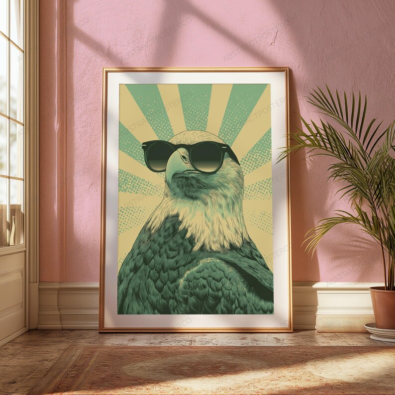 May include: A framed wall art print featuring a stylized illustration of a bald eagle wearing black sunglasses. The eagle is depicted in shades of green and cream against a sunburst background with a dotted texture pattern in a retro graphic style.