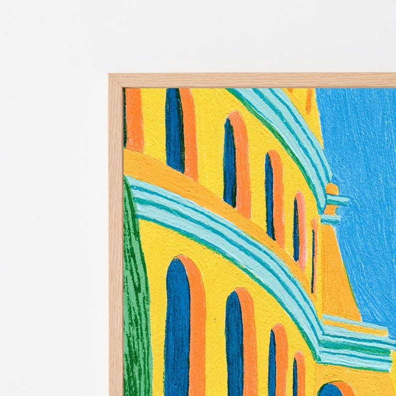 May include: A framed painting featuring a yellow building with arched blue windows and orange accents, set against a bright blue sky. The artwork displays visible brushstrokes and a textured surface, enclosed within a light-coloured wooden frame.