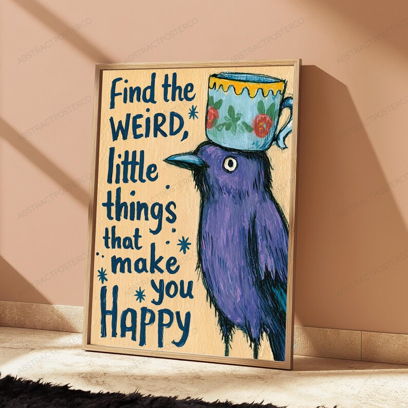 Op de afbeelding: Een ingelijste kunstprint op een lichte houten achtergrond met een paarse vogel met een blauw bloemrijk theekopje op zijn kop. De tekst luidt: Find the WEIRD, little things that make you Happy, geaccentueerd met kleine blauwe sterretjes.