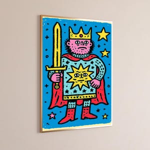 May include: A framed wall art print featuring a stylized illustration of a king with a pink face, wearing a yellow crown and a blue tunic decorated with a large yellow sun and black stars. The figure holds a yellow sword and wears a red cape.