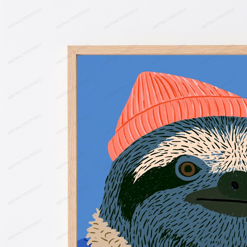 May include: A framed wall art print featuring a stylized illustration of a sloth wearing a bright coral-colored beanie. The sloth has dark blue fur, a cream-colored face, and a dark brown eye, set against a solid blue background.