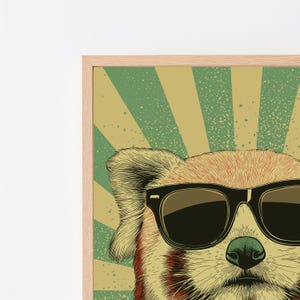 May include: A framed wall art print featuring a stylized illustration of a red panda wearing black sunglasses. The background consists of alternating light green and tan sunburst rays with a speckled texture throughout the entire design.