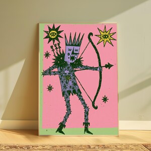 K&ouml;nnte beinhalten: Ein rechteckiger Wandkunstdruck mit einer violetten Figur mit Krone, die einen Bogen und einen Pfeil h&auml;lt. Die Figur befindet sich vor einem rosa Hintergrund mit gr&uuml;nen R&auml;ndern, umgeben von schwarzen Stern- und Augenmotiven in texturiertem Grafikstil.
