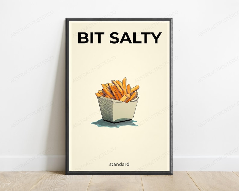 K&ouml;nnte beinhalten: Ein gerahmter Kunstdruck mit cremefarbenem Hintergrund und schwarzem Rahmen. Der Text BIT SALTY steht oben in Schwarz, das Wort standard unten. Eine zentrale Illustration zeigt goldbraune Pommes frites in einem wei&szlig;en Beh&auml;lter.