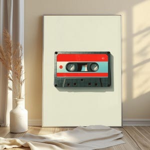 May include: A framed wall art print featuring a centered graphic of a vintage cassette tape. The tape has a dark gray lower casing, a bright red upper section, and a light blue central band. The number 62 is printed in white on the top right.