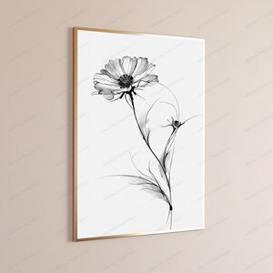 May include: A framed wall art print featuring a black and white botanical illustration of a single cosmos flower with delicate, wispy petals and a slender stem. The artwork is presented in a thin, metallic gold frame against a neutral wall.
