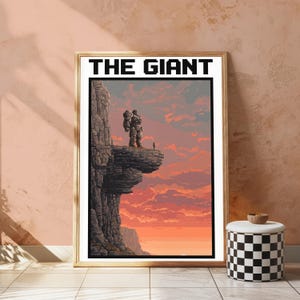 May include: A framed pixel art print titled THE GIANT, featuring a large stone-like figure standing on a cliff edge next to a small person, set against a vibrant orange and pink sunset sky with rocky terrain in a vertical rectangular composition.