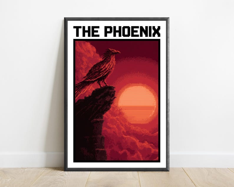 Puede incluir: Una impresi&oacute;n de arte de p&iacute;xeles enmarcada titulada THE PHOENIX, que muestra un p&aacute;jaro oscuro posado en un acantilado irregular sobre un gran sol naranja brillante contra un cielo rojo profundo y nublado. La obra est&aacute; en un marco negro.