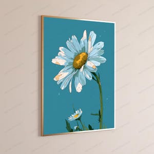 May include: A rectangular wall art print in a thin gold frame featuring a stylized illustration of a large white daisy with a textured yellow center and a smaller daisy below, set against a solid teal blue background with subtle white specks.