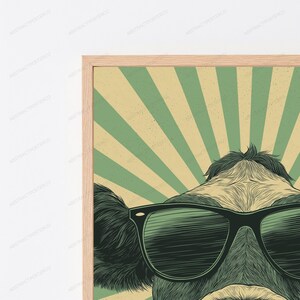 May include: A framed wall art print featuring a stylized illustration of a cow wearing black sunglasses. The background consists of alternating light green and beige sunburst rays. The cow has dark fur and is centered in the frame.