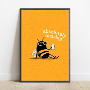 May include: A framed wall art print featuring a yellow background with a black and yellow bee wearing white sunglasses and holding a silver can. The text "absolutely buzzing" is printed in white above the bee, which is sitting down.