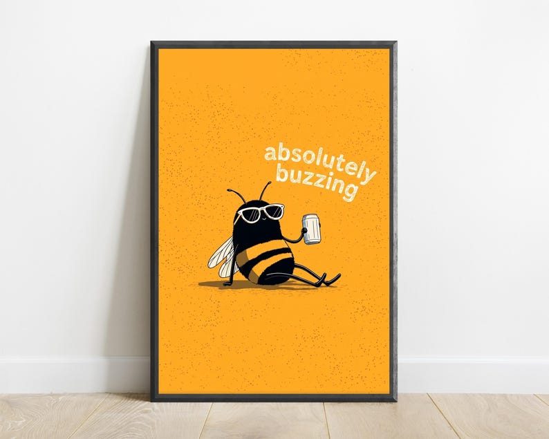 May include: A framed wall art print featuring a yellow background with a black and yellow bee wearing white sunglasses and holding a silver can. The text "absolutely buzzing" is printed in white above the bee, which is sitting down.