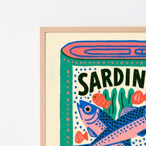 May include: A framed art print featuring a stylized illustration of a sardine tin. The design includes a green border, a blue lid, and the text SARDIN in black. The graphic depicts several fish in shades of blue and pink against a cream background.