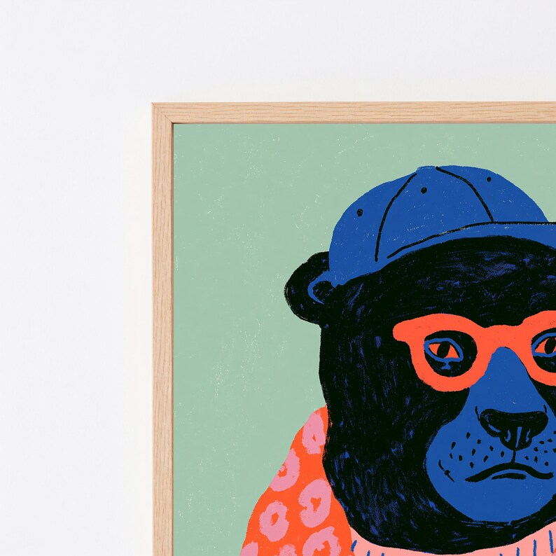 May include: A framed wall art print featuring a stylized black bear wearing a bright blue baseball cap and vibrant orange glasses. The bear is set against a solid light green background and wears a pink patterned garment around its neck.