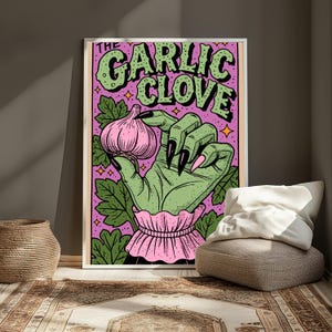 Pu&ograve; includere: Una stampa artistica da parete rettangolare che raffigura una mano verde con lunghe unghie nere che tiene un bulbo d'aglio rosa. Lo sfondo &egrave; viola con foglie verdi e piccole stelle arancioni. Il testo THE GARLIC CLOVE &egrave; stampato in grandi lettere verdi.