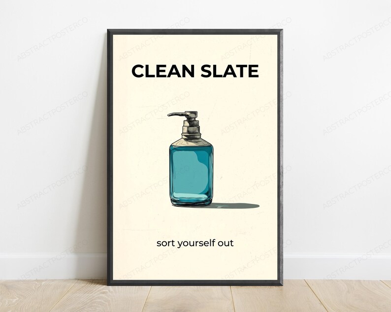 May include: A framed wall art print featuring a light cream background with a central illustration of a blue liquid soap dispenser. The text CLEAN SLATE appears in black at the top, and the text sort yourself out appears in black at the bottom.
