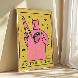 Puede incluir: Una impresi&oacute;n rectangular enmarcada que muestra una figura rosa con orejas puntiagudas sosteniendo una aguja grande y un p&aacute;jaro peque&ntilde;o sobre un fondo amarillo. La obra incluye contornos verde oscuro, estrellas y el texto A STITCH IN TIME.