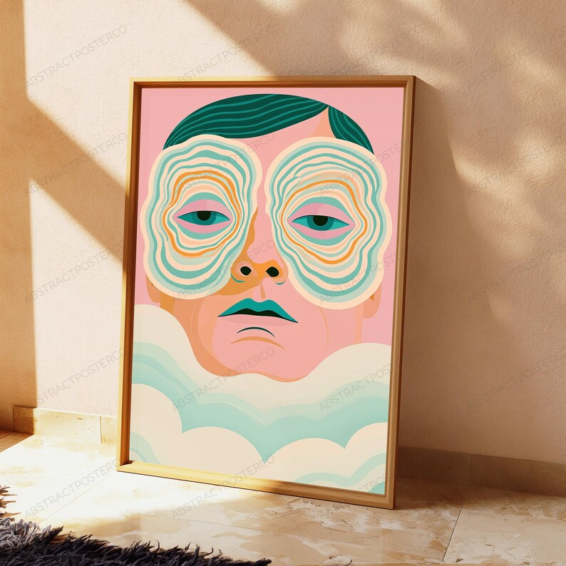May include: A framed vertical art print featuring a stylized human face with dark teal hair. The eyes are surrounded by concentric, wavy rings in shades of teal, orange, and cream. The lips are teal, and the lower portion of the face is obscured by soft, pale blue and cream cloud-like shapes against a solid pink background.