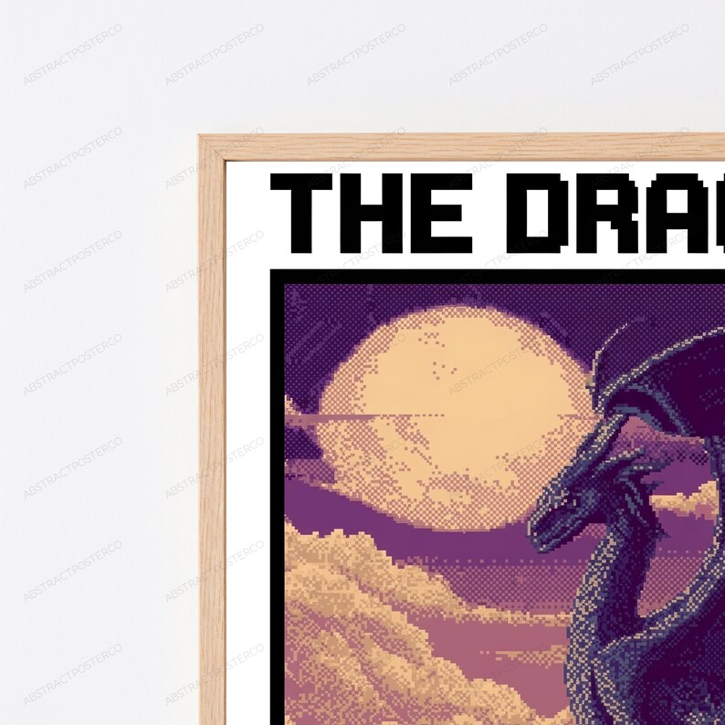 May include: A framed pixel art print featuring a dark purple dragon silhouette against a large, pale yellow moon and a cloudy sky. The text THE DRA is visible in black pixelated font at the top of the white-bordered print within a light wood frame.