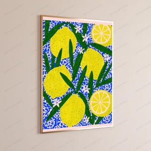 K&ouml;nnte beinhalten: Ein gerahmter, rechteckiger Wandkunstdruck mit einem lebendigen Muster aus gelben Zitronen, gr&uuml;nen Bl&auml;ttern und kleinen wei&szlig;en Bl&uuml;ten vor einem leuchtend blauen Hintergrund mit einem sich wiederholenden wei&szlig;en Blumenmotiv. Der Druck hat einen hellrosa Rand.