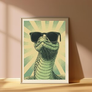 May include: A framed wall art print featuring a detailed illustration of a green snake wearing black sunglasses. The snake is positioned centrally against a background of radiating light green and cream-colored sunburst rays in a vintage style.