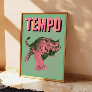 May include: A framed wall art print featuring a light green background with a pink tiger illustration rendered in a halftone dot pattern. The word TEMPO is printed in large, bold pink letters with black drop shadows at the top of the rectangular print.