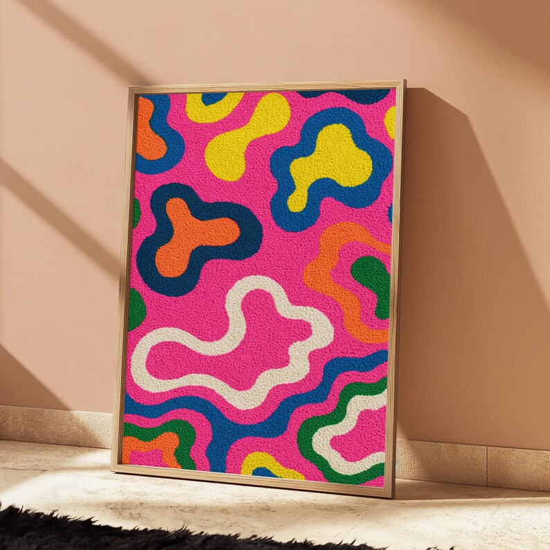 May include: A rectangular wall art piece featuring a textured, tufted surface with a vibrant, abstract pattern of amoeba-like shapes in bright pink, yellow, orange, green, white, and dark blue, all enclosed within a light-coloured wooden frame.