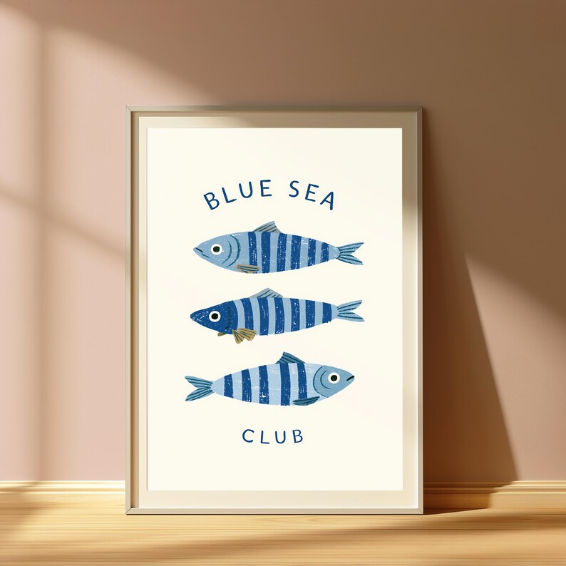 Pode incluir: Uma impress&atilde;o art&iacute;stica emoldurada apresentando tr&ecirc;s peixes orientados horizontalmente com listras verticais azuis e azul-claras. O texto "BLUE SEA" est&aacute; impresso em azul escuro acima dos peixes e a palavra "CLUB" est&aacute; abaixo deles.