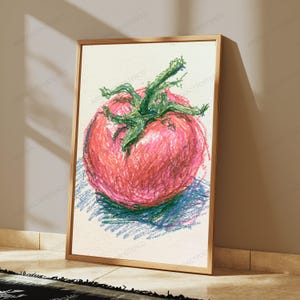 May include: A framed wall art print featuring a crayon-style drawing of a single red tomato with a green stem and leaves. The artwork uses visible, textured strokes in shades of red, green, and blue against a light, off-white background.