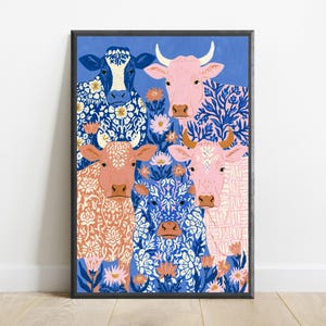 May include: A framed art print featuring four cows against a blue background. The cows are decorated with intricate white and blue floral patterns. The artwork includes pink, orange, and blue flowers interspersed among the cows in a flat illustration style.