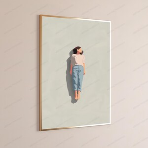 May include: A framed wall art print featuring a minimalist illustration of a figure lying flat on a light beige background. The figure wears a pale pink short-sleeved top and light blue trousers, with a dark shadow cast directly beneath them.