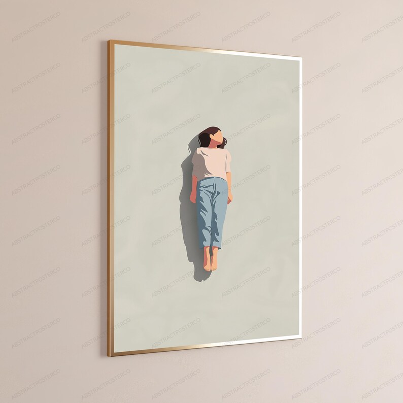 May include: A framed wall art print featuring a minimalist illustration of a figure lying flat on a light beige background. The figure wears a pale pink short-sleeved top and light blue trousers, with a dark shadow cast directly beneath them.