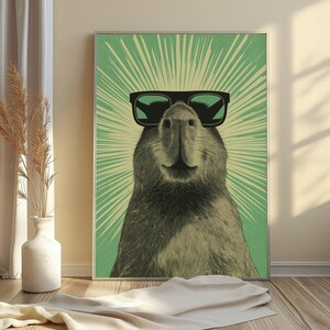 Peut inclure: Une affiche murale rectangulaire repr&eacute;sentant une illustration centr&eacute;e d'un capybara portant des lunettes de soleil noires. Le fond est de couleur vert clair avec des lignes blanches rayonnantes partant de l'animal, cr&eacute;ant un effet soleil.